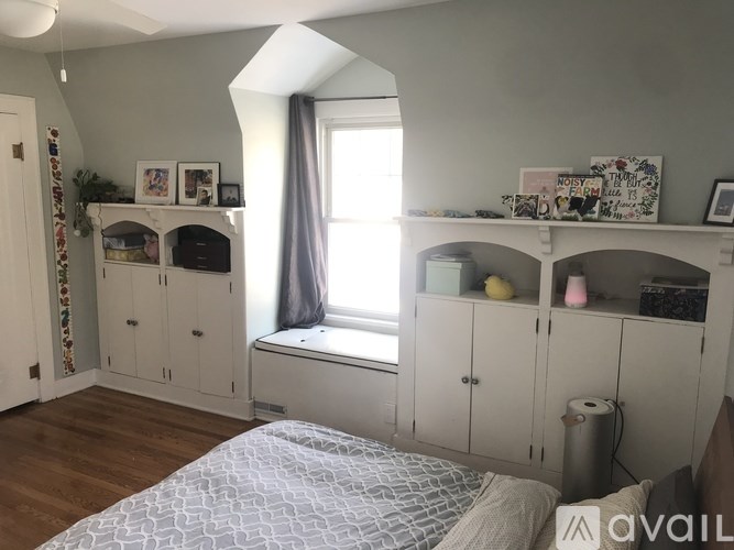 A bedroom with a bed, a window with a curtain, and a shelf with various items.