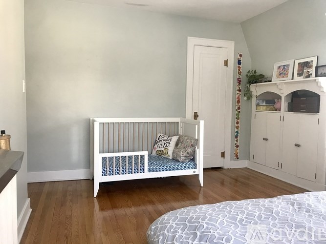 A white crib with a blue and white patterned bedspread sits in a room with wooden floors.