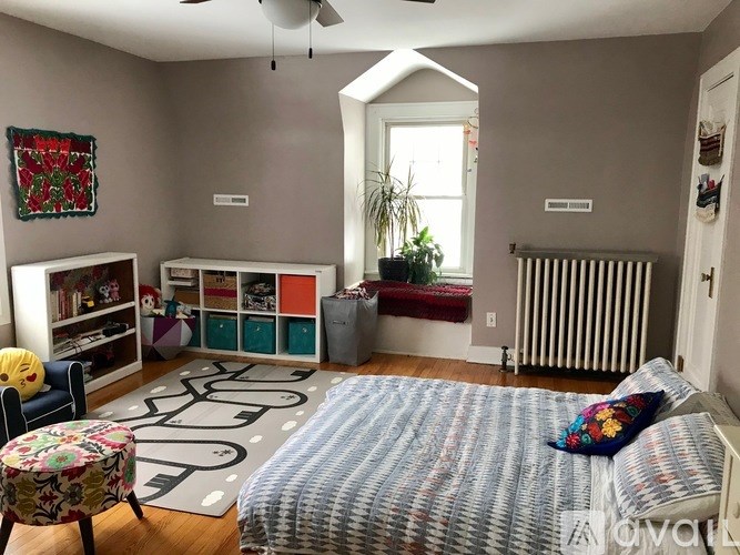 A bedroom with a bed, a chair, a window, and a radiator.
