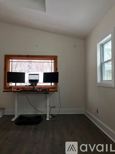 A room with a desk and two monitors in front of a window.