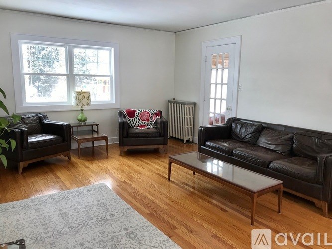 A living room with a black leather couch and a grey rug.