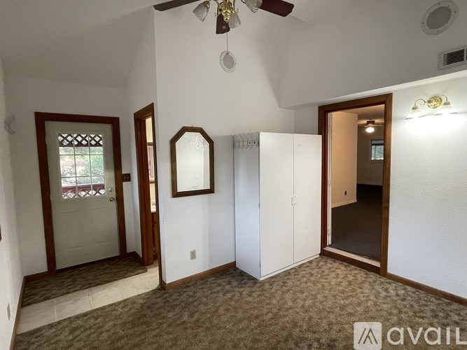 A room with a carpeted floor, a ceiling fan, and a door leading to another room.