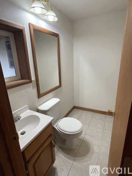 A bathroom with a toilet, sink, mirror and wooden cabinet.