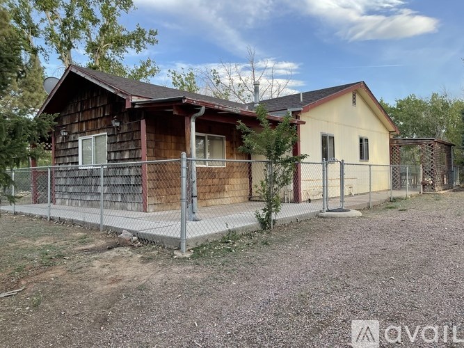 A house with a brown roof and a yellow house with a red roof are behind a fence.
