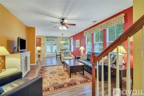 A living room with a brown rug and a ceiling fan.