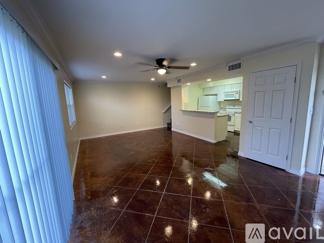 A room with a ceiling fan and a kitchen area in the background.
