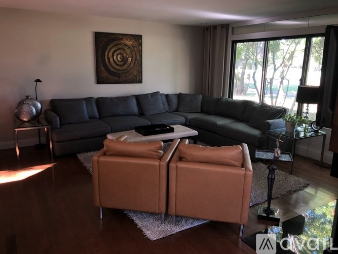 A living room with a black leather sofa and a tan ottoman.