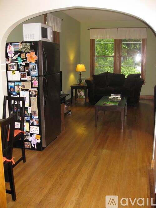 A black fridge with many magnets on it in a room with a black couch and a table.