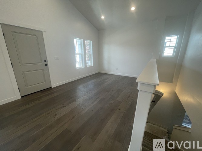 A room with wooden floors and white walls, with a door and two windows.