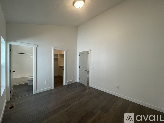 A room with white walls and wooden flooring, with a door on the left and two open doors in the middle of the room.