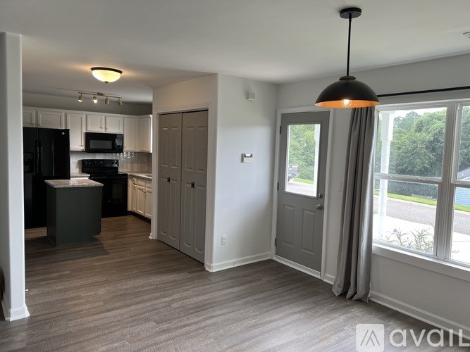 A kitchen with a black fridge and microwave, wooden floors, and a large window with a view of the outside.