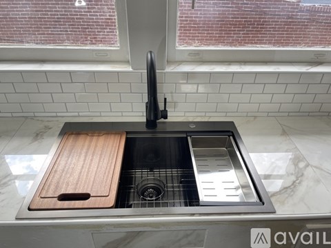 A kitchen sink with a wooden cutting board and a black faucet.