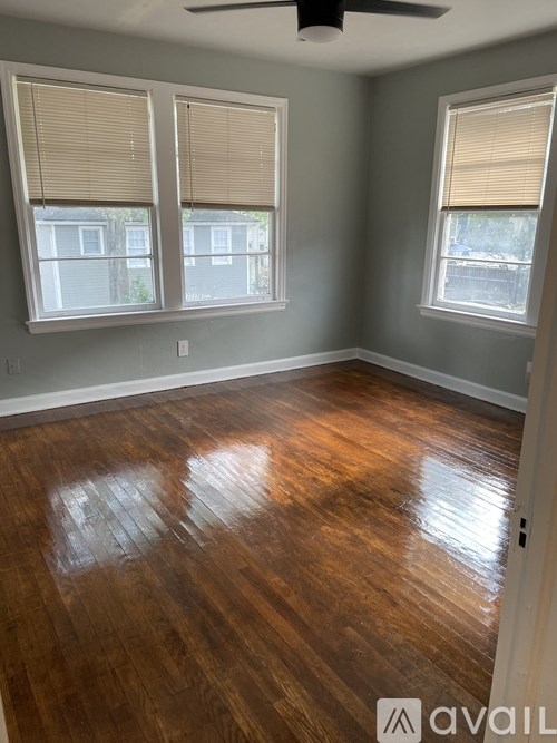 A room with wooden floors and two windows with blinds.