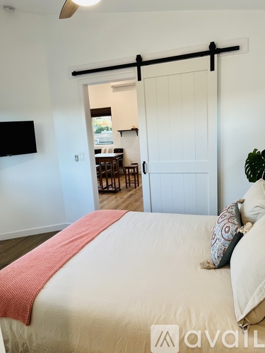 A bedroom with a bed, a television, and a sliding door leading to a kitchen.