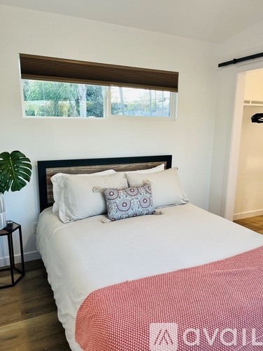A bedroom with a large bed and a window with blinds.