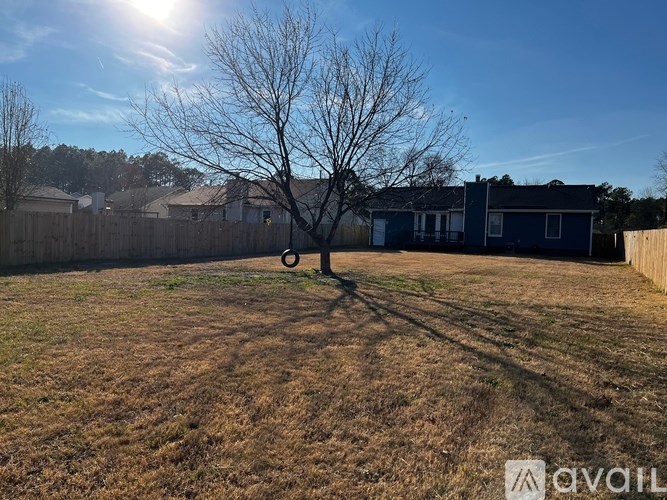A tree stands in a yard with a house in the background.