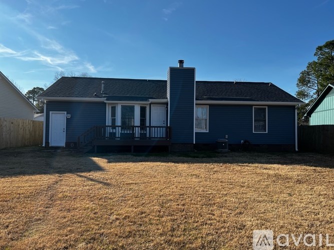 A blue house with a white door and windows is surrounded by a fence and has a chimney.