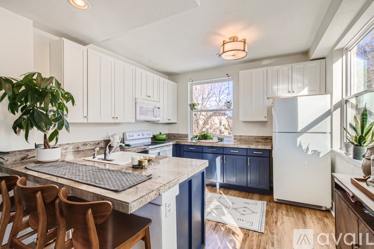 A kitchen with a white fridge, wooden chairs and a marble counter top.