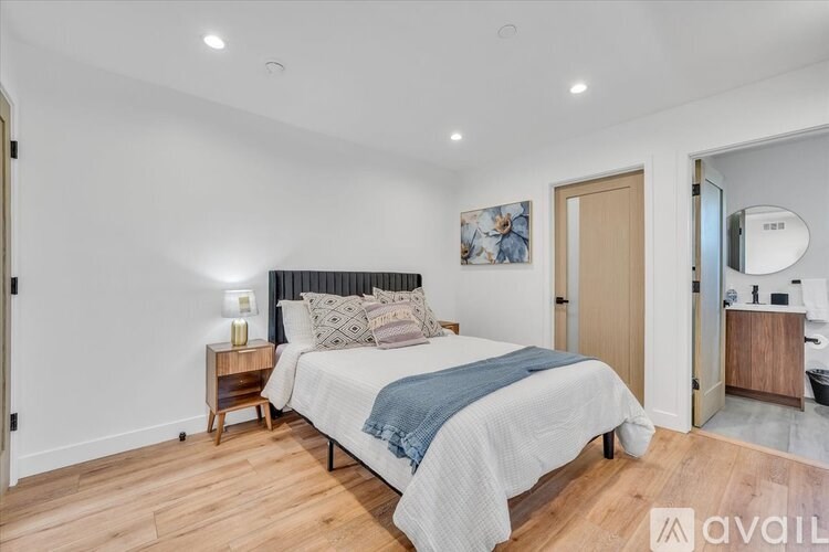 A bedroom with a bed, nightstand, and a painting on the wall.