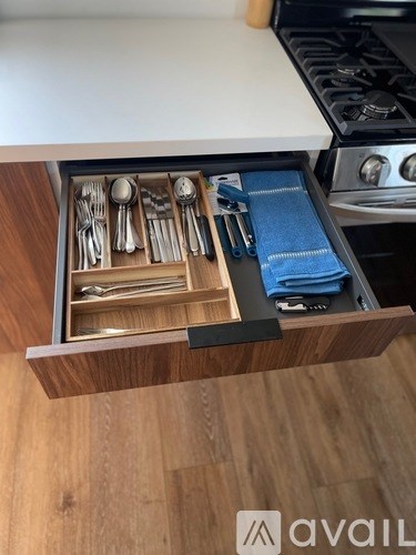A drawer with utensils and a blue towel is open.