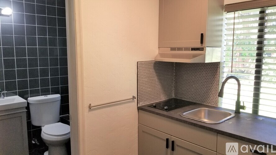 A kitchen with a sink, toilet, and a window with blinds.