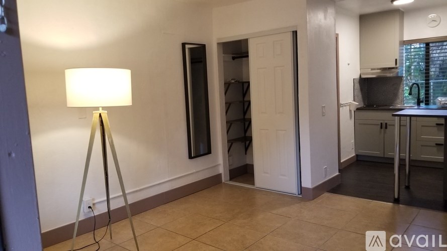 A room with a lamp on a tripod and a door open to a kitchen.