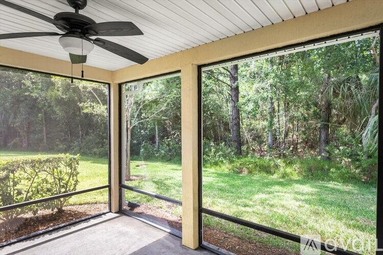 A room with a ceiling fan and sliding glass doors that open to a forest.