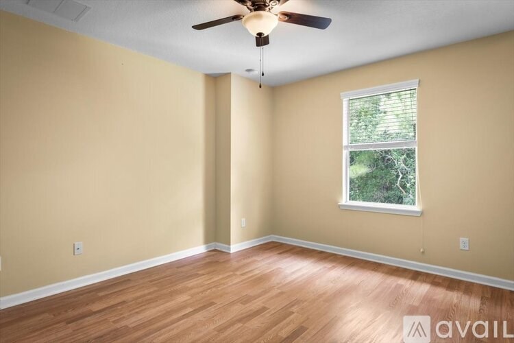 A room with a ceiling fan and a window showing greenery outside.