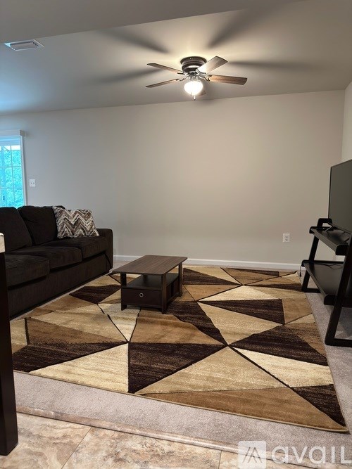 A living room with a black couch and a brown and beige rug.