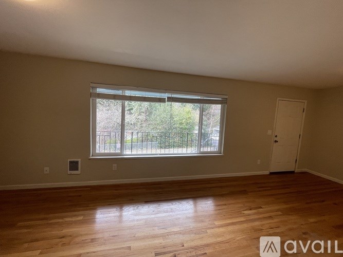 Empty room with wooden flooring and a window overlooking a fence.