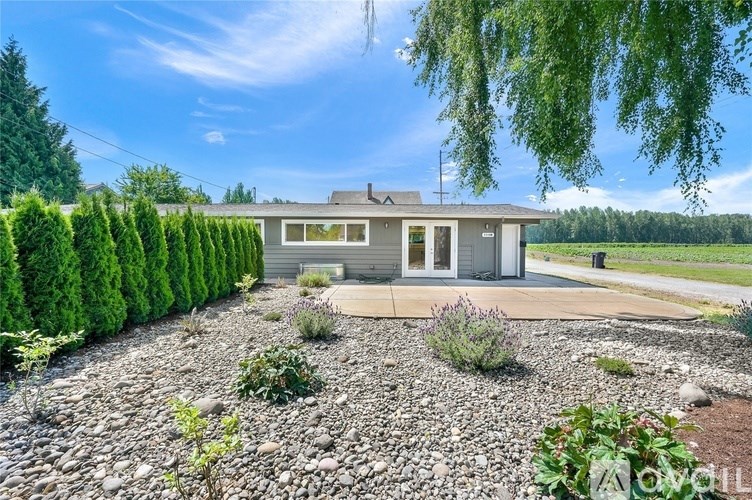 A small house with a grey roof and a gravel driveway in front.