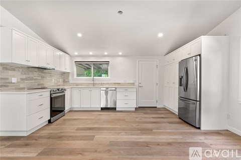 A modern kitchen with white cabinets and a wooden floor.
