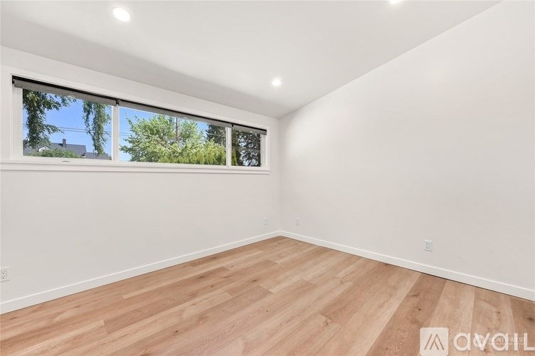 A room with wooden flooring and a window showing trees and a house outside.