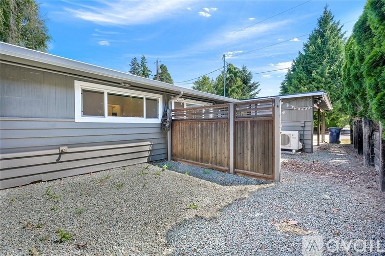 A gravel driveway leads to a wooden fence and a house.