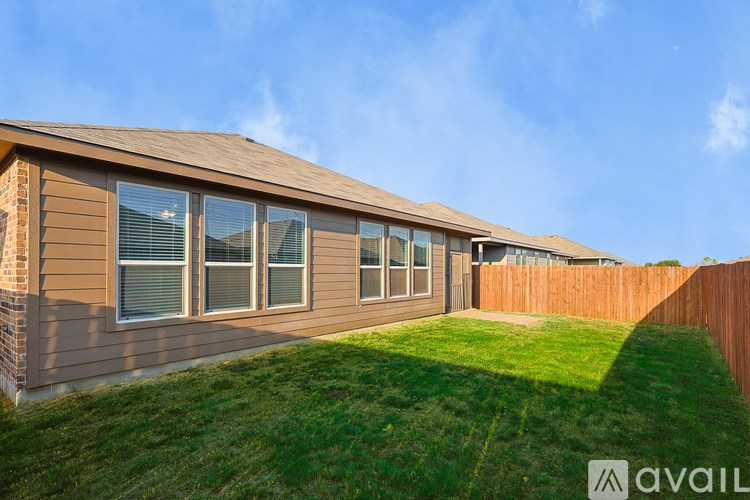 A house with a brown siding and a brown roof with a fence and green grass in front.