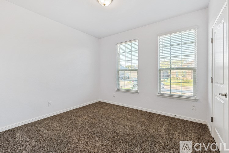 A room with a carpeted floor, two windows with blinds, and a door.