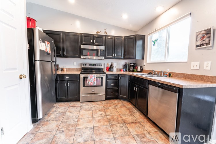 A kitchen with black appliances and brown tile flooring.