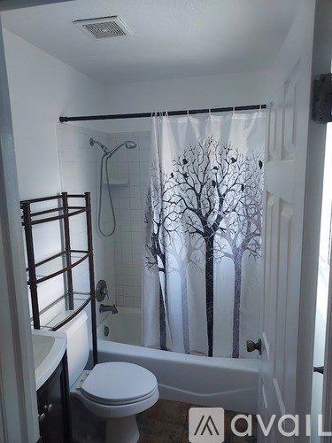 A bathroom with a white toilet and a shower curtain with a tree design.