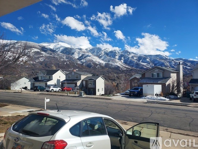 A silver car is parked on a street with houses and snowy mountains in the background.