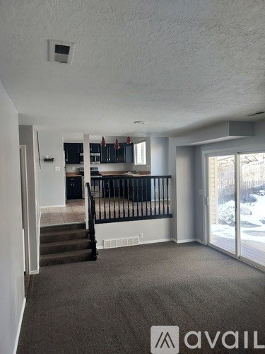 A carpeted room with a staircase leading to a kitchen.