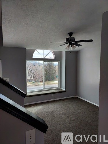 A room with a ceiling fan and a window overlooking a street.