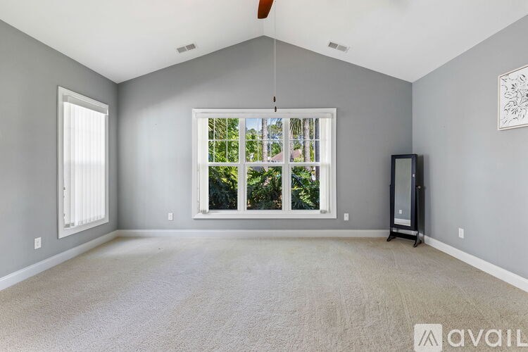 A spacious room with a carpeted floor, a window with a view of greenery outside, and a wall-mounted artwork.