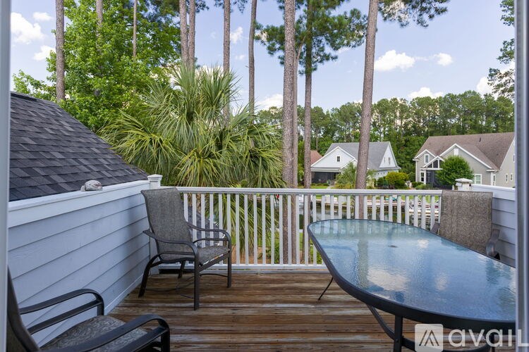 A wooden deck with a glass table and chairs overlooking a residential area.