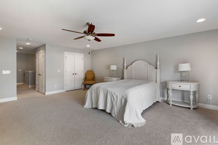 A bedroom with a bed, desk, and fan.