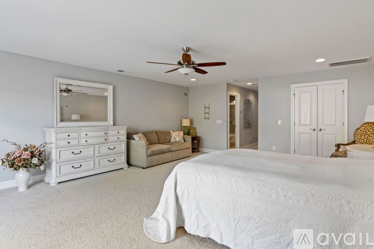 A bedroom with a large bed, a dresser, a mirror, a couch, and a ceiling fan.