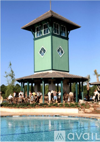 A group of people are sitting at tables under a green tower by a pool.