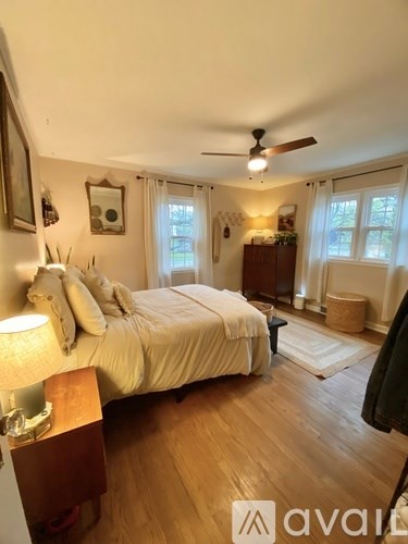 A bedroom with a bed, a ceiling fan, and a window with white curtains.