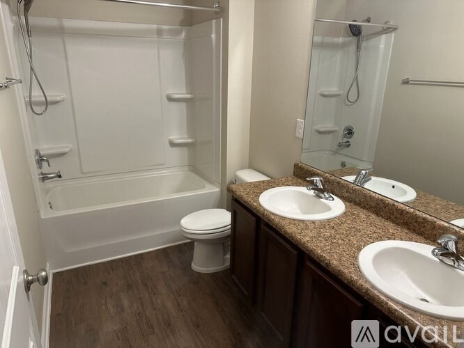 A bathroom with a white tub and toilet, a sink with a mirror above it, and a wooden floor.