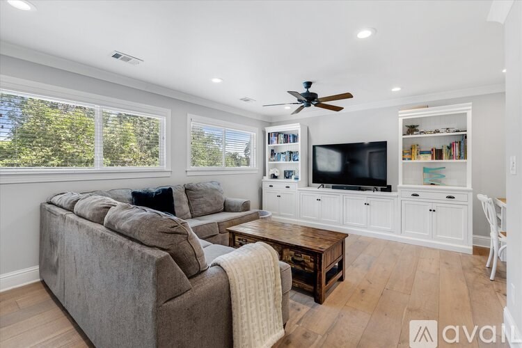 A living room with a grey couch, a wooden coffee table, a television, and a ceiling fan.