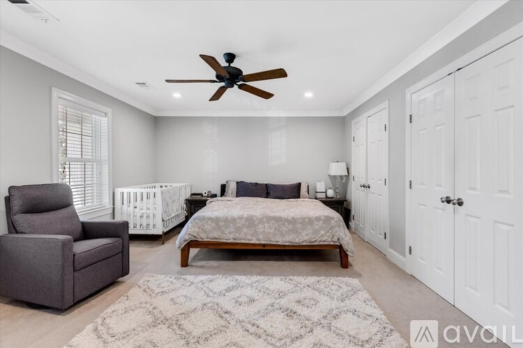 A bedroom with a bed, a crib, a chair, and a rug.